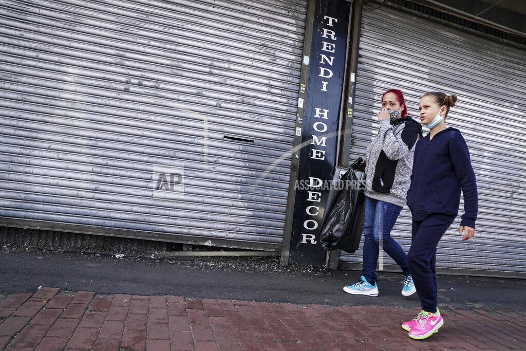 John Minchillo Pedestrians pass shuttered storefronts on Thursday, Oct. 15, 2020, as restrictions are imposed due to a COVID-19 infection increase in the Far Rockaway neighborhood of the borough of Queens in New York. After shutdowns swept entire nations during the first surge of the coronavirus earlier this year, some countries and U.S. states are trying more targeted measures as cases rise again around the world. (AP Photo/John Minchillo)