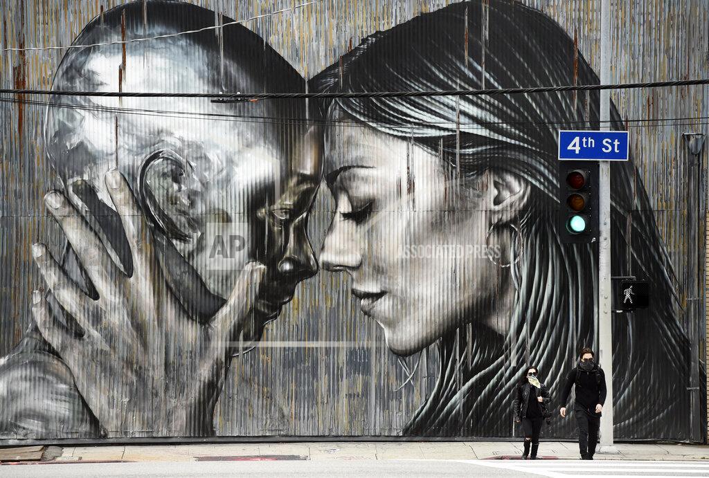 Chris Pizzello People wear masks as they cross the street in front of a mural in the Arts District of Los Angeles, as stay-at-home orders continue in California due to the coronavirus, Friday, April 10, 2020. (AP Photo/Chris Pizzello)