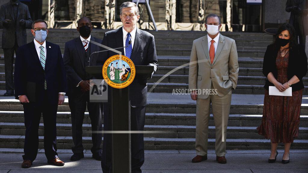 North Carolina Gov. Roy Cooper, center, and lawmakers gather Wednesday, March 10, 2021, for a news conference to announce that leaders of the Republican-led state legislature and the governor have reached an agreement to reopen the state's K-12 public schools to full-time daily instruction in Raleigh. (Juli Leonard/The News & Observer via AP)