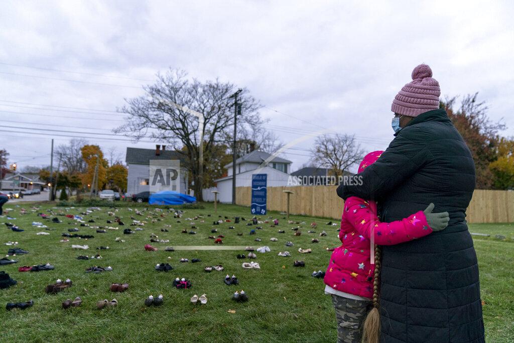 David Goldman Theresa McGarity, left, embraces her granddaughter, Blake, 8, while remembering her mother, Carolyn Wilson, during an art installation vigil with shoes representing residents in Macomb County who died from COVID-19 in Mount Clemens, Mich., Friday, Oct. 30, 2020. Wilson, who died in April at 76 years old, was a God-fearing woman and had been teaching Blake how to crochet. On Friday night, as McGarity brought Blake to the art installation, a raucous pro-Trump demonstration down the street could be heard as they read the age and hometown of each of their dead. (AP Photo/David Goldman)