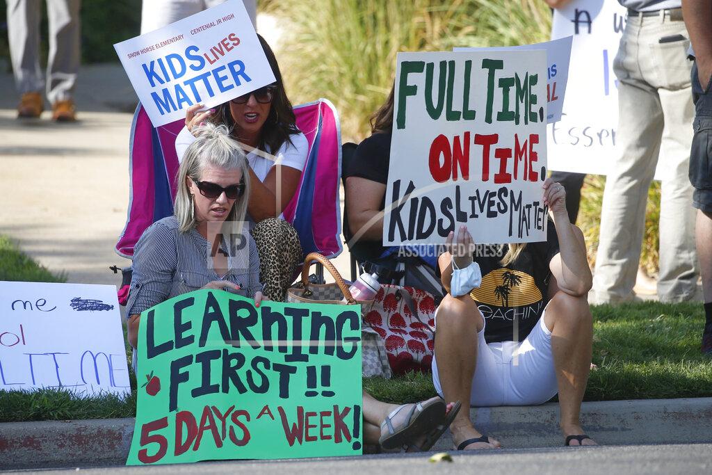 Rick Bowmer Staci Patrick, left, protests with others in front of the Davis School District Office, Tuesday, Aug. 4, 2020, in Farmington, Utah. A group of parents protested the district's hybrid reopening plan because they would prefer their children to attend school five days a week. (AP Photo/Rick Bowmer)