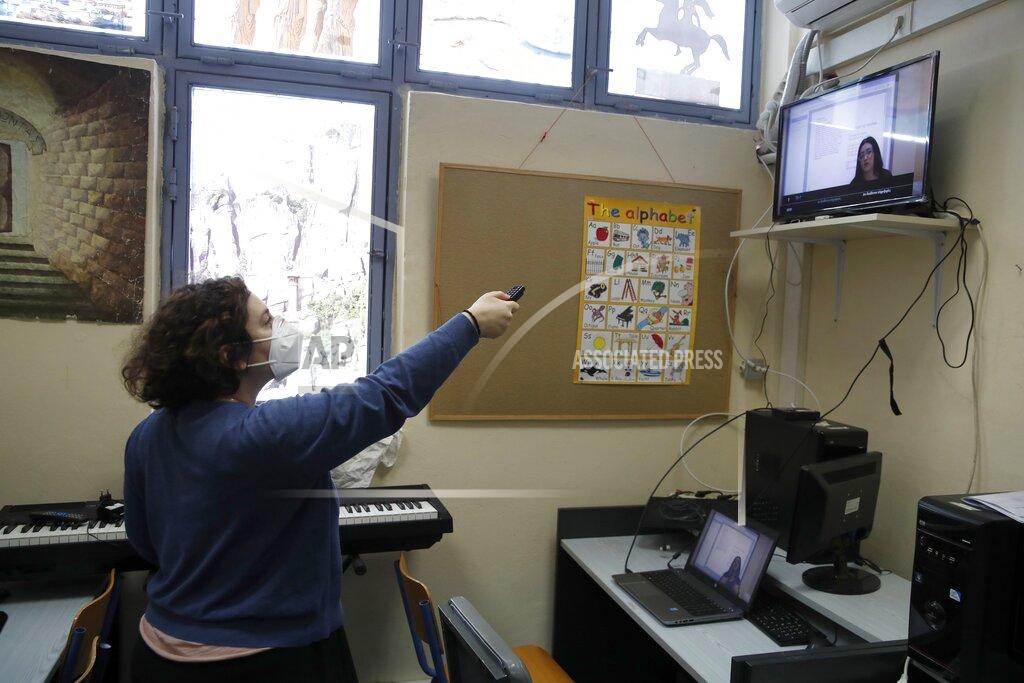 Computer teacher Evi Kontopoulou uses a remote control to find "Prospathodas TV," or "Trying TV," the channel of Avlona's prison school, north of Athens, Wednesday, Feb. 10, 2021. With Greece's schools shut due to the pandemic, all lessons have gone online. But the online world isn't within reach of everyone _ and particularly not within reach of the students of Avlona Special Youth Detention Center, where internet devices are banned by law from the cells. (AP Photo/Thanassis Stavrakis)
