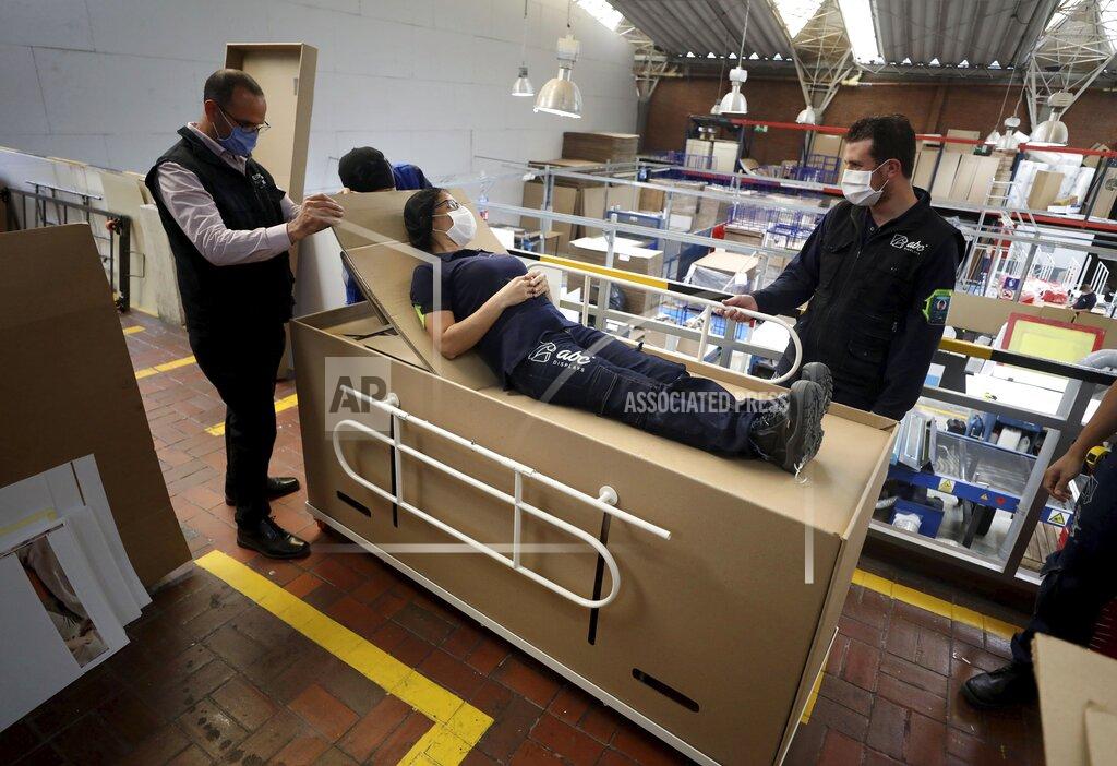 Fernando Vergara Rodolfo Gomez, left, and his employees demonstrate how their design of a cardboard box can serve as both a hospital bed and a coffin, designed for COVID-19 patients, in Bogota, Colombia, Friday, May 8, 2020. Gomez said he plans to donate the first units to Colombia's Amazonas state, and that he will sell others to small hospitals for 87 dollars. (AP Photo/Fernando Vergara)