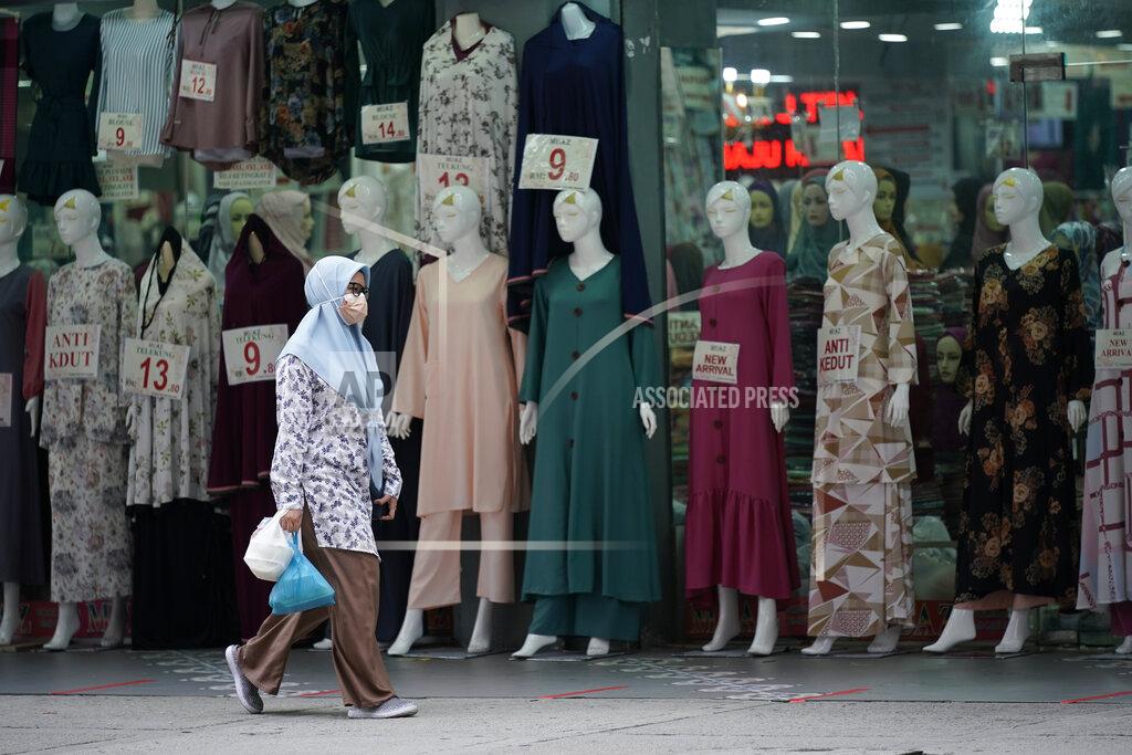 Vincent Thian In this Friday, April 19, 2021, photo, a woman wearing a protective mask passes a clothing shop in the Ramadan bazaar in Kuala Lumpur, Malaysia. Malaysian Prime Minister Muhyiddin Yassin announced Monday that the whole country will be placed under a near lockdown for about a month but all economic sectors will be allowed to operate. (AP Photo/Vincent Thian)