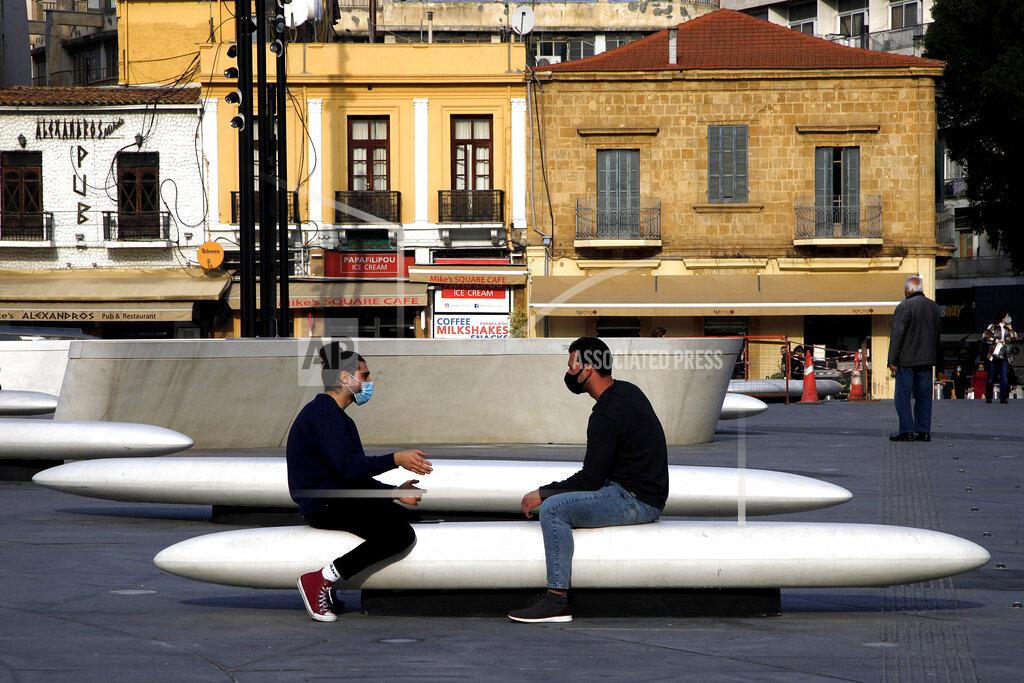 Petros Karadjias Men wearing face masks to prevent the spread of coronavirus talk on a bench at Elefphtheria, Liberty, square in central Nicosia, Friday, Jan. 8, 2021. Cyprus is returning to lockdown mode for the remainder of the month with daytime restrictions on movement and a shuttering of schools after the country's health minister conceded that a raft of tough measures already in place including a night-time curfew weren't enough to curtail the spread of the coronavirus. (AP Photo/Petros Karadjias)