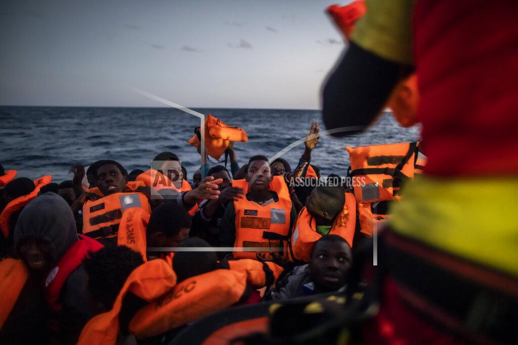 14-year old Bamba Bourahima from Ivory Coast, centre, waits to receive a life vest as rescuer Alberto Agrelo distributes them to all the migrants aboard an overcrowded rubber boat after being rescued by the Spanish NGO Open Arms rescue vessel in the Mediterranean Sea, international waters, at 80 miles off the Libyan coast, Saturday Feb. 13, 2021. Various African migrants drifting in the Mediterranean Sea after fleeing Libya on unseaworthy boats have been rescued. In recent days, the Libyans had already thwarted eight rescue attempts by the Open Arms, a Spanish NGO vessel, harassing and threatening its crew in international waters. (AP Photo/Bruno Thevenin)