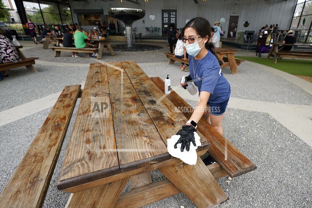 David J. Phillip Hostess Carla Alexander disinfects a table at the Saint Arnold Brewing Company, Friday, June 26, 2020, in Houston. Texas Gov. Greg Abbott announced Friday that he is shutting bars back down and scaling back restaurant capacity to 50%, in response to the increasing number of COVID-19 cases in Texas. (AP Photo/David J. Phillip)