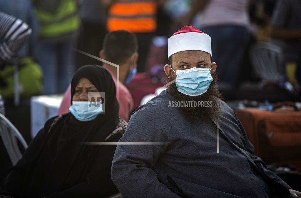 Khalil Hamra Palestinians wearing face masks sit next to their luggage, as they wait to cross to the Rafah crossing border with Egypt, southern Gaza Strip, Sunday, Sept. 27, 2020. (AP Photo/Khalil Hamra)