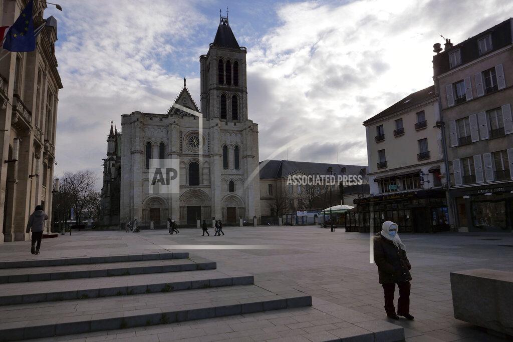 Christophe Ena A woman walks past the Saint-Denis Basilica, a burial place for French kings entombed, north of Paris, Monday, Jan. 25, 2021. Many people lining up for vaccines in the Paris suburb are particularly grateful for the injections. The surrounding region is the poorest in mainland France, with 130 languages spoken and the country's highest rise in mortality last spring. (AP Photo/Christophe Ena)