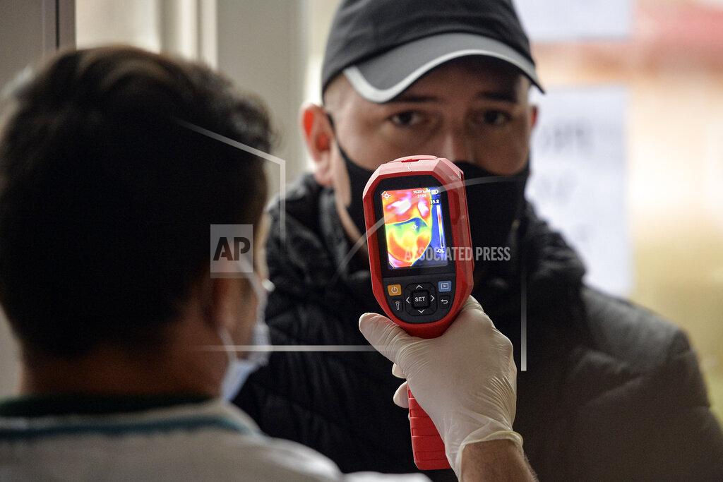 Alexandru Dobre An election official measures the body temperature of a voter in Dragomiresti Vale, Romania, Sunday, Dec. 6, 2020. Voting started in Romania's legislative election expected to restore some measure of stability after five years of political and social turbulence with more than 18 million Romanians registered to vote for a new legislative body. (AP Photo/Alexandru Dobre)