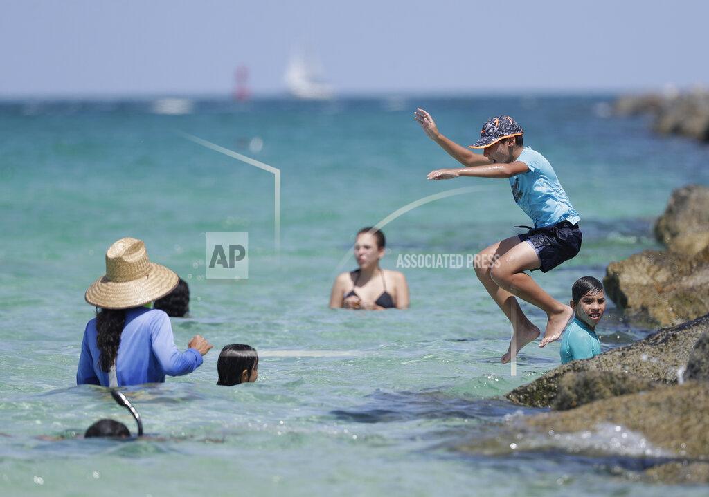 Wilfredo Lee A young beach goer jumps off the rocks of a jetty, Tuesday, June 30, 2020, on Miami Beach, Florida's famed South Beach. Beaches in Miami-Dade County will be closed from Friday, July 3 through Monday, July 6. (AP Photo/Wilfredo Lee)