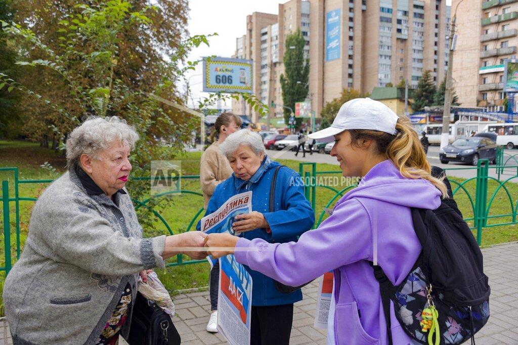 Uncredited A volunteer of Luhansk regional election commission, right, distributes newspapers to local citizens prior to a referendum in Luhansk, Luhansk People's Republic controlled by Russia-backed separatists, eastern Ukraine, Thursday, Sept. 22, 2022. Authorities in Russian-controlled regions in eastern and southern Ukraine are preparing to hold referendums on becoming part of Russia's a move that could allow Moscow to escalate the war. The votes start Friday in the Luhansk, Kherson and partly Russian-controlled Zaporizhzhia and Donetsk regions. Writing on newspaper reads in Russian "27.09 Yes." (AP Photo)