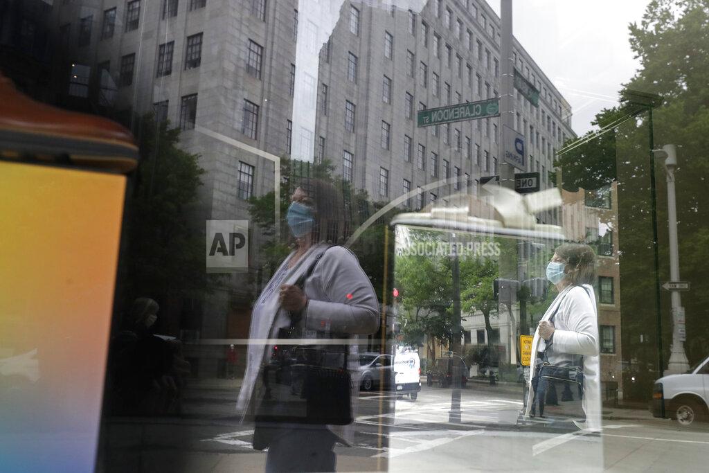 Steven Senne FILE - In this June 11, 2020, file a passer-by wears a mask out of concern for the coronavirus while walking past a storefront window in Boston. Eighty-five percent of Democrats call economic conditions “poor,” while 65% of Republicans describe them as “good,” according to a new survey by The Associated Press-NORC Center for Public Affairs Research. (AP Photo/Steven Senne, File)