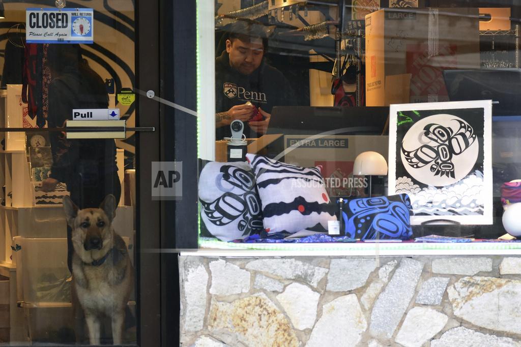Peter Segall A dog stands at the door of the Trickster Company store on Front Street in downtown Juneau, Alaska, while people unload boxes on Friday, April 24, 2020. Some businesses have been able to keep the online side of their businesses operating even as their doors remain closed to the public. (Peter Segall/Juneau Empire via AP)