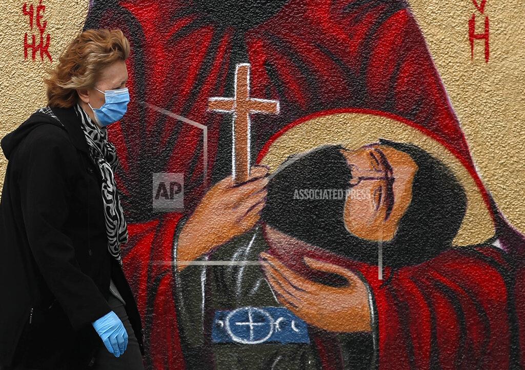 A woman wearing a protective face mask passes by graffiti depicting a Christian Orthodox icon in Belgrade, Serbia, Wednesday, May 27, 2020. (AP Photo/Darko Vojinovic)