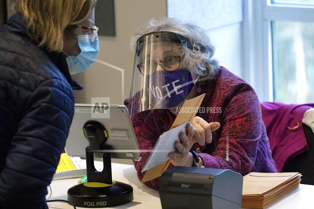 Steven Senne FILE - In this Oct. 28, 2020, file photo, poll worker Alice Machinist, of Newton, Mass., right, wears a mask and shield out of concern for the coronavirus while assisting a voter, left, with a ballot during early in-person general election voting at the Newton Free Library, in Newton, Mass. The 2020 presidential election had all the makings of a looming disaster: fears of Russian meddling, violence at the polls, voter intimidation and poll workers fleeing their posts over the coronavirus. But the election was largely smooth, in large part because 107 million voters that cast their ballots early and took the pressure off Election Day operations. (AP Photo/Steven Senne, File)