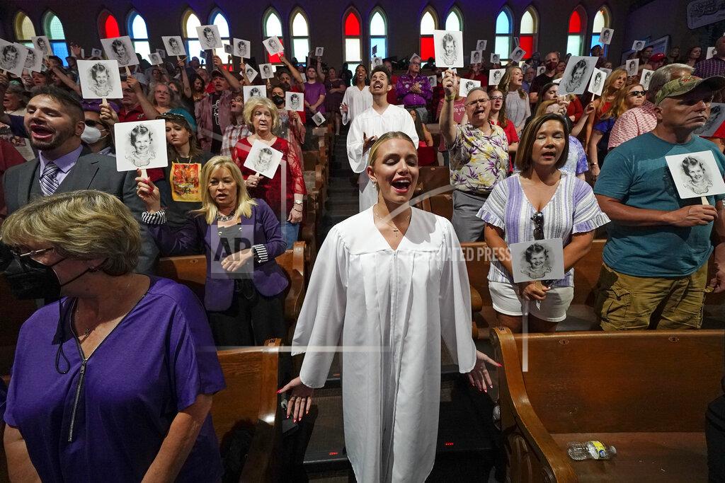 Mark Humphrey A church choir and spectators sing "Love Can Build A Bridge," along with Wynonna Judd during a tribute to country music star Naomi Judd in the Ryman Auditorium, Sunday, May 15, 2022, in Nashville, Tenn. The fans that the spectators hold show a picture of Naomi Judd as a child. Naomi Judd died April 30. She was 76. (AP Photo/Mark Humphrey)