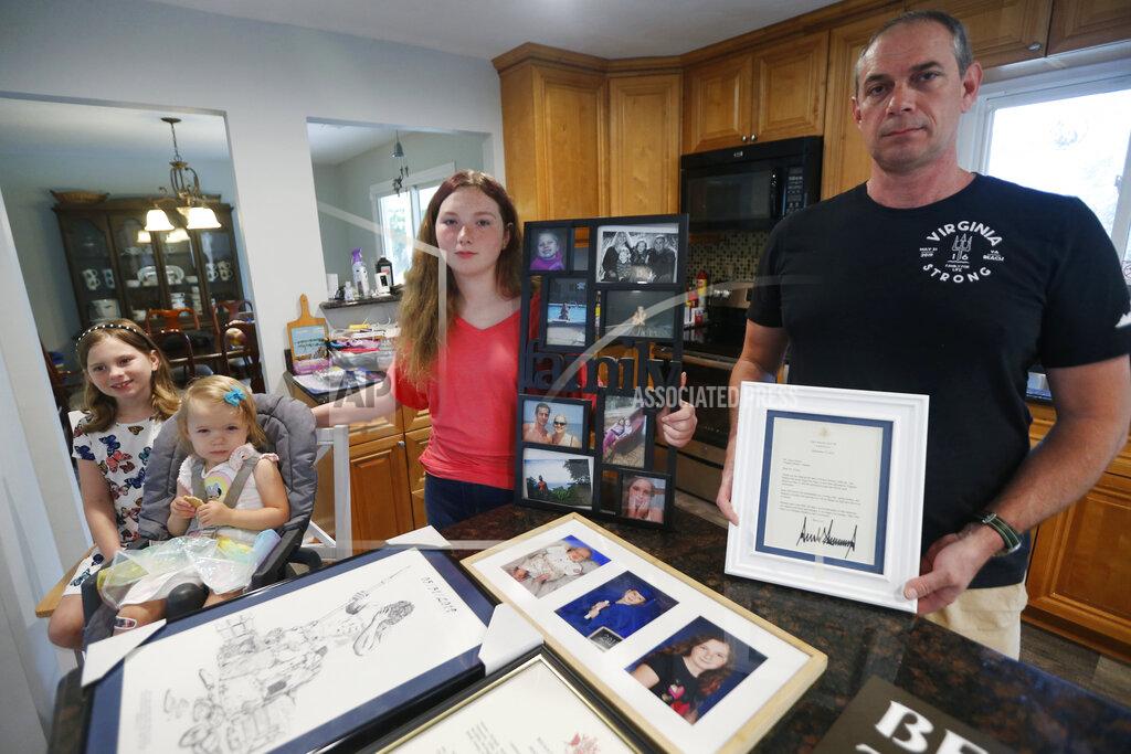 Steve Helber In this May 22, 2020, photo, Jason Nixon, right, holds a letter from President Donald Trump as he poses with his children, Mackenzie, left, Madilyn, second from left and Morgan as they display memorabilia from last years shooting that took the life of Kate Nixon at their home in Virginia Beach, Va. As the shooting's one-year anniversary approaches this weekend, some of the victim's family members say the rampage is effectively forgotten. (AP Photo/Steve Helber)