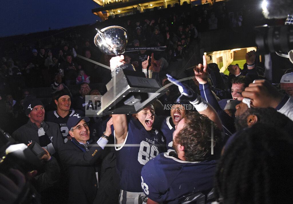 Arnold Gold FILE - In this Nov. 23, 2019, file photo, Yale's JP Shohfi, center, holds the Ivy League championship trophy during a celebration with teammates after their 50-43 doubl- overtime victory against Harvard in an NCAA college football game at the Yale Bowl in New Haven, Conn. At left is Yale University president Peter Salovey. The Ivy League was the first conference to scuttle its basketball postseason when the pandemic broke out during March Madness a year and a half ago. It was the first Division I conference to suspend fall sports in July 2020. Now the schools are getting back on the field the same way they left: cautiously. (Arnold Gold/New Haven Register via AP, File)