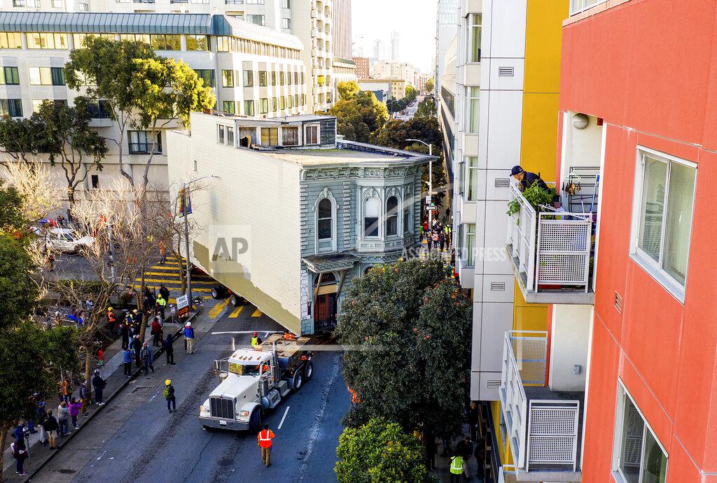 Noah Berger A man watches from a balcony as a truck pulls a Victorian home through San Francisco on Sunday, Feb. 21, 2021. The house, built in 1882, was moved to a new location about six blocks away to make room for a condominium development. According to the consultant overseeing the project, the move cost approximately $200,000 and involved removing street lights, parking meters, and utility lines. (AP Photo/Noah Berger)