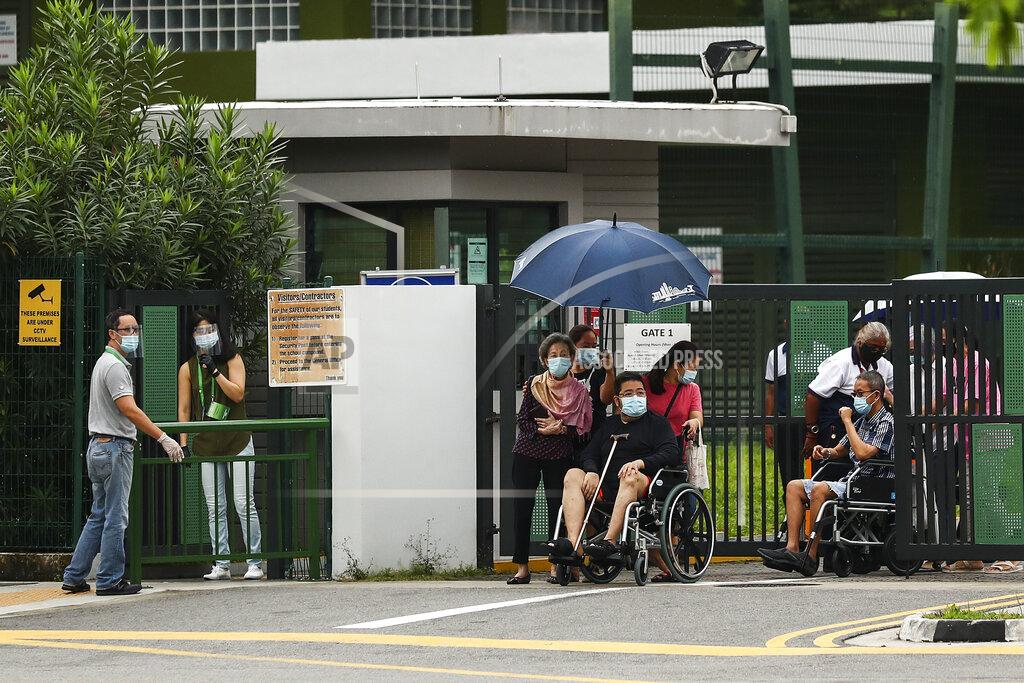 Wheelchair-bound voters, wearing face masks, leave the Alexandra Primary School polling center after casting their votes in Singapore, Friday, July 10, 2020. Wearing masks and plastic gloves, Singaporeans began voting in a general election that is expected to return Prime Minister Lee Hsien Loong's long-governing party to power. (AP Photo)