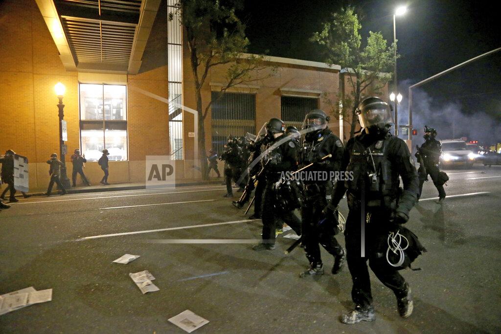 Beth Nakamura Portland police declare a riot at the Multnomah County Building, on Tuesday, Aug. 18, 2020, in Portland, Ore. Protesters in Portland broke out the windows of a county government building, sprayed lighter fluid inside and set a fire in a demonstration that started Tuesday night and ended Wednesday morning with clashes with police, officials said. (Beth Nakamura/The Oregonian via AP)