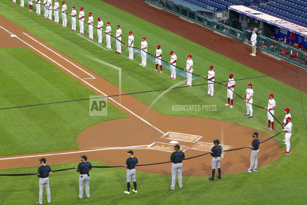 Charles Fox The Philadelphia Phillies, top, and the Miami Marlins hold a black ribbon in honor of the Black Lives Matter movement and in memory of George Floyd, before a baseball game Friday, July 24, 2020, in Philadelphia. Major League Baseball has already postponed a second scheduled game between Miami and Baltimore after more than a dozen Marlins players and staff tested positive for the coronavirus, prompting the club to lock down in Philadelphia. Commissioner Rob Manfred said the soonest the Marlins could resume their schedule is Wednesday, when they are set to play in Baltimore. (Charles Fox/The Philadelphia Inquirer via AP)