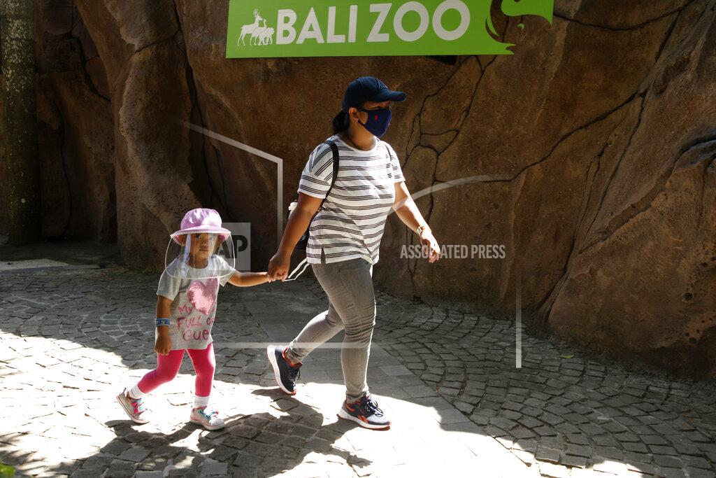 Firdia Lisnawati A mother walks with her daughter wearing protective gear during their visit to the zoo in Bali, Indonesia, Monday, July 13, 2020. Indonesia's resort island of Bali reopened after a three-month virus lockdown last week, allowing local people and stranded foreign tourists to resume public activities before foreign arrivals resume in September. (AP Photo/Firdia Lisnawati)