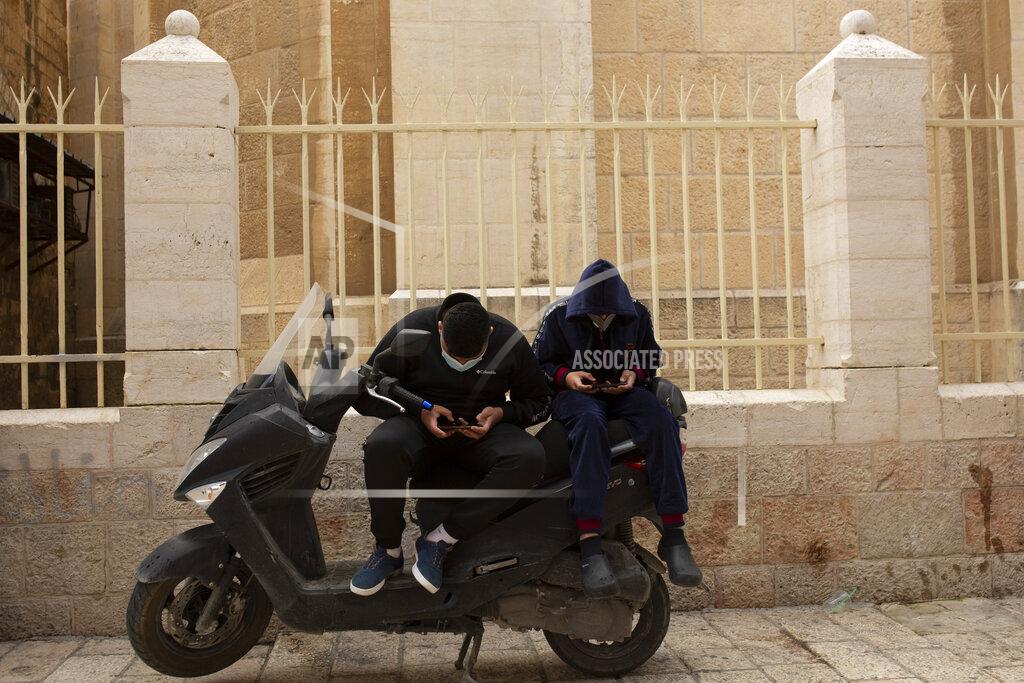 Young men scroll on their smart phones in the Old City of Jerusalem, Wednesday, Dec. 23, 2020. In the early days of the pandemic, a panicked Israel began using a mass surveillance tool on its own people, tracking civilians’ mobile phones to halt the spread of the coronavirus. But months later, the tool’s effectiveness is being called into question and critics say its use has come at an immeasurable cost to the country’s democratic principles. (AP Photo/Maya Alleruzzo)