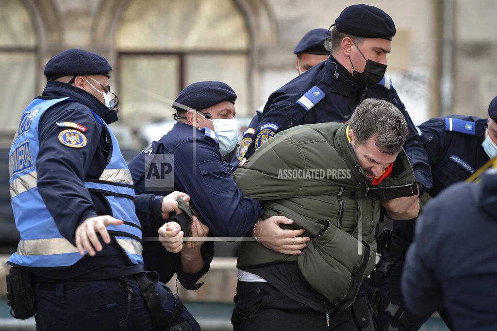 Alexandru Dobre Four Romanian riot police officers struggle to detain a protester against COVID-19 restrictions before people gathered for a rally joined by thousands in Bucharest, Romania, Monday, March 29, 2021. Thousands of anti-restriction protesters took to the streets in several cities across Romania on Monday evening, a day after new restriction measures came into force. (AP Photo/Alexandru Dobre)
