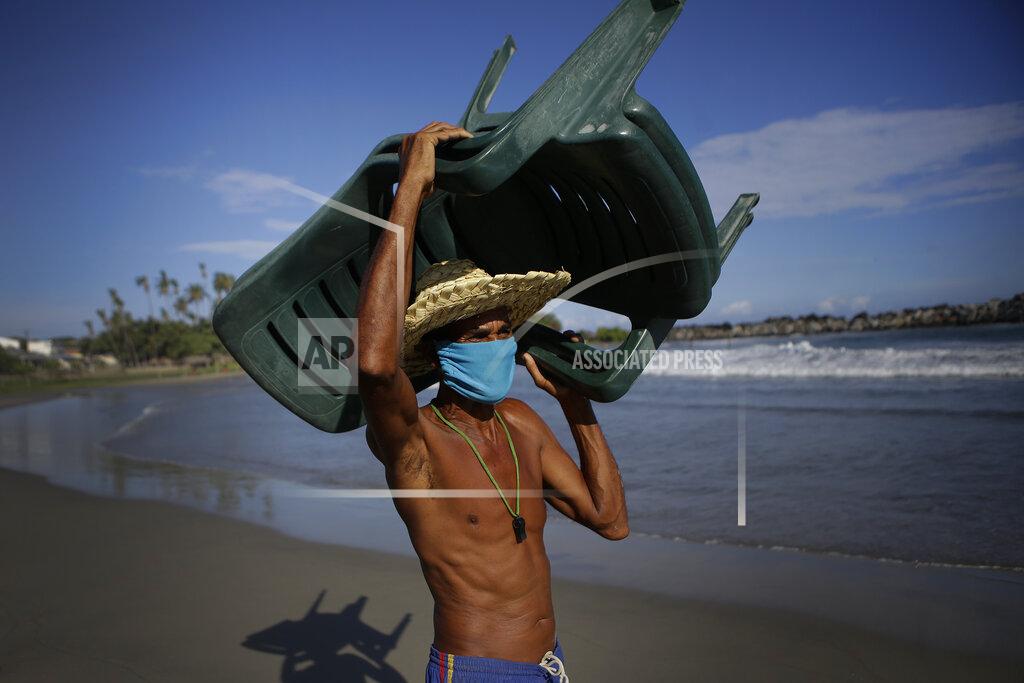 Matias Delacroix Douglas Yriarte carries rental chairs for tourists on the La Ultima beach which was closed for months amid the COVID-19 pandemic in La Guaira, Venezuela, Friday, Oct. 23, 2020. Strict quarantine restrictions forced the closure of beaches across the country in March and reopened this week in hopes of revitalizing the battered economy. (AP Photo/Matias Delacroix)