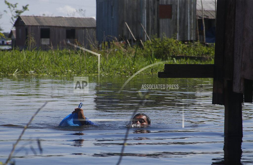 Edmar Barros Francisco Fabiano Rodrigues takes a bag with fish to his home keeping his head bearly above water on a street flooded by the rise of the Negro river in Iranduba, Amazonas state, Brazil, Monday, May 23, 2022. The Amazon region is being hit hard by flooding with 35 municipalities that are facing one of their worst floods in years and the water level is expected to rise over the coming months. (AP Photo/Edmar Barros)