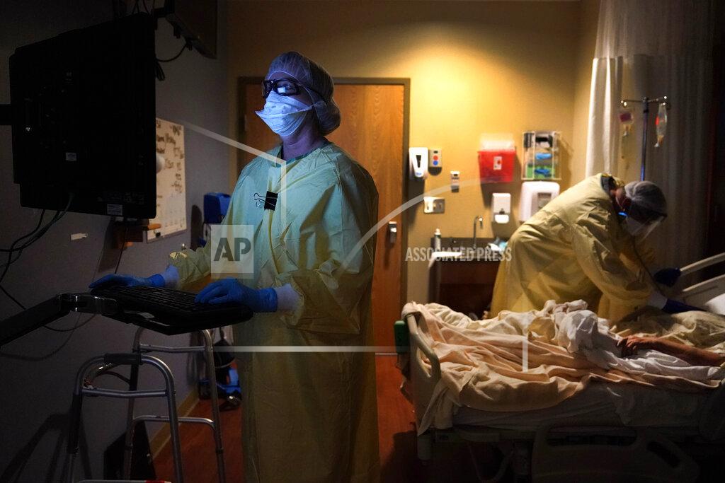 Jeff Roberson Registered nurse Shelly Girardin, left, is illuminated by the glow of a computer monitor as Dr. Shane Wilson examines COVID-19 patient Neva Azinger inside Scotland County Hospital on Tuesday, Nov. 24, 2020, in Memphis, Mo. The coronavirus pandemic largely hit urban areas first, but the autumn surge is now ravaging rural America, stressing the staffs of tiny hospitals like the one in Scotland County. (AP Photo/Jeff Roberson)