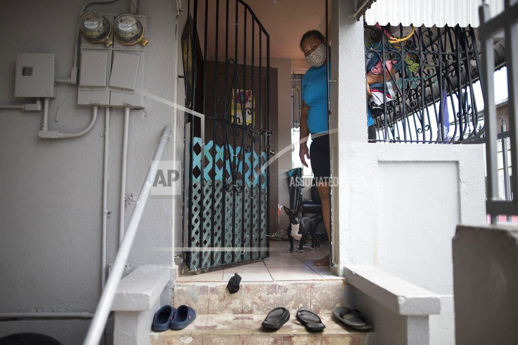 Delia Vicente, an unemployed mother of two boys whose husband is hospitalized with a bacterial infection and unable to work as a debris collector, peeks out of the doorway of her house, where she and her family remove their shoes before entering, during the Covid-19 pandemic, in San Juan, Puerto Rico, Wednesday, April 29, 2020. Puerto Rico's government is refusing to open school cafeterias amid a coronavirus pandemic as a growing number of unemployed parents struggle to feed their children. (AP Photo/Carlos Giusti)