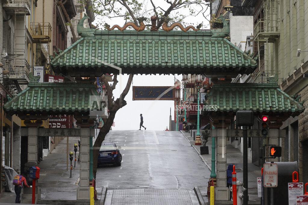 Jeff Chiu FILE - In this April 4, 2020, file photo, a pedestrian crosses Grant Street behind the Dragon Gate, an entrance to Chinatown in San Francisco. San Francisco reached the least-restrictive yellow tier for a brief period in October, the only urban area to do so, before an alarming surge in cases forced a retreat. Los Angeles never emerged from the most restrictive tier until March 2021. (AP Photo/Jeff Chiu, File)