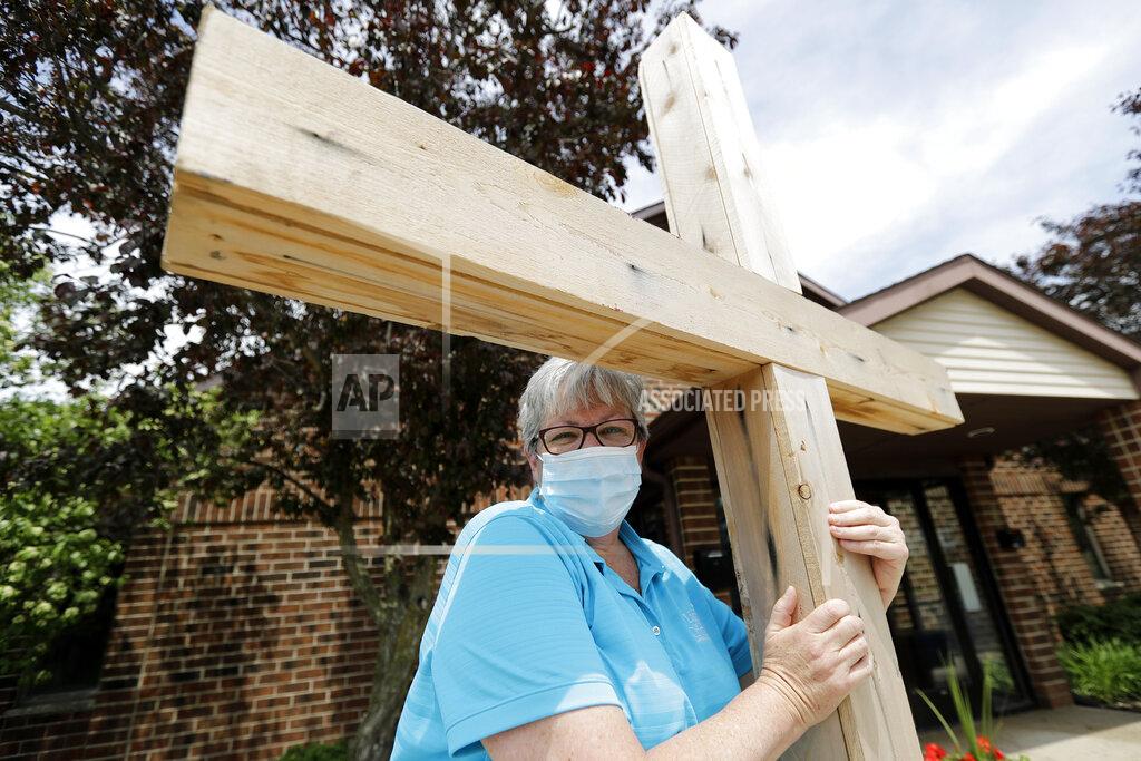 Nam Y. Huh Associate Pastor Sharon Rogers poses for a portrait with a cross at Light of Christ Lutheran Church in Algonquin, Ill., Sunday, May 24, 2020. “The church is not a building, the church is people,” said Rogers, explaining why parents had embraced the idea of an outdoor service for their children's upcoming confirmation ceremony. (AP Photo/Nam Y. Huh)