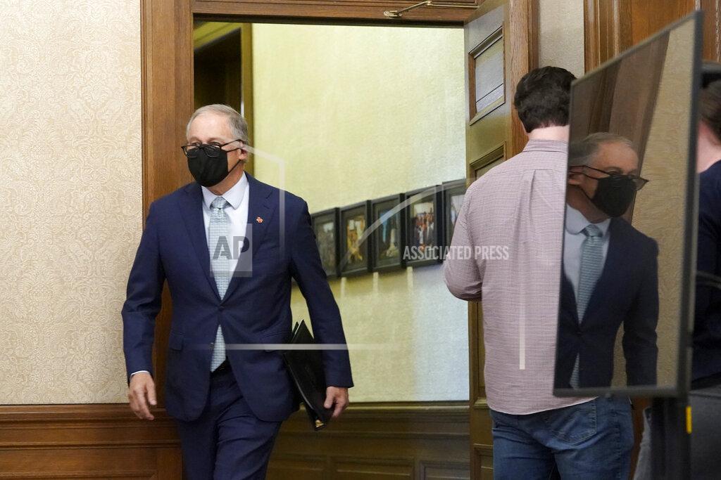 Ted S. Warren Washington Gov. Jay Inslee is reflected in a video monitor as he walks past a staff member while arriving to speak at a news conference, Tuesday, Jan. 5, 2021, at the Capitol in Olympia, Wash. Inslee said some COVID-19 restrictions in Washington will be eased beginning next week and the state will change its reopening plan to move from a county-based oversight system to one focused on regions. (AP Photo/Ted S. Warren)