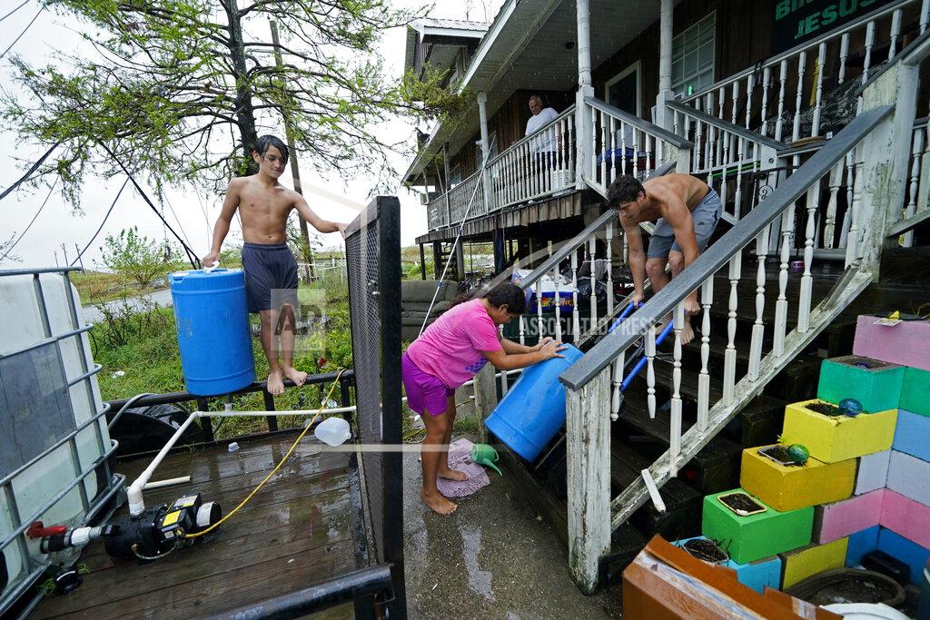 Gerald Herbert Lerryn Brune, 10, center, Terren Dardar, 17, right, and Dayton Verdin, 14, move barrels of rainwater they collected from Tropical Storm Nicholas, in the aftermath of Hurricane Ida in Pointe-aux-Chenes, La., Tuesday, Sept. 14, 2021. They have had no running water since the hurricane, and collected 140 gallons of rainwater in two hours from the tropical storm, which they filter and pump into their house for showers. (AP Photo/Gerald Herbert)