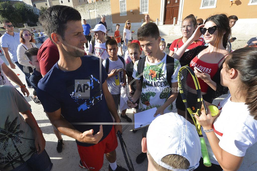 Zvonko Kucelin In this photo taken June 18, 2020, Serbian tennis player Novak Djokovic, left, talks to children in Zadar, Croatia. Novak Djokovic has tested positive for the coronavirus after taking part in a tennis exhibition series he organized in Serbia and Croatia. (AP Photo/Zvonko Kucelin)