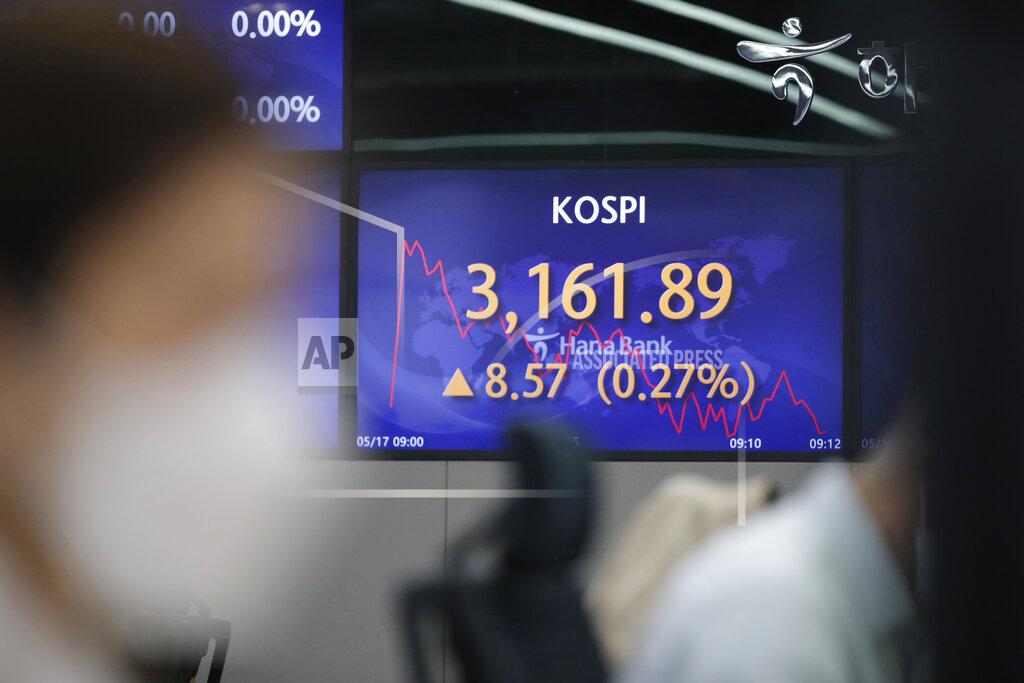 A currency trader watches computer monitors near a screen showing the Korea Composite Stock Price Index (KOSPI) at a bank's foreign exchange dealing room in Seoul, South Korea, Monday, May 17, 2021. Asian stock markets were mixed Monday after Taiwan and Singapore tightened anti-coronavirus restrictions and Wall Street turned in its biggest weekly decline in three months. (AP Photo/Lee Jin-man)