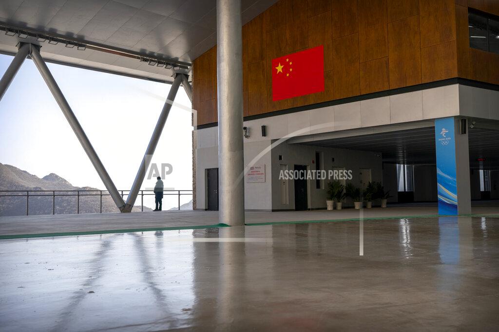 Mark Schiefelbein A staff member stands at a balcony near a Chinese flag at the National Sledding Center in Yanqing on the outskirts of Beijing, Friday, Feb. 5, 2021. Beijing Olympic organizers showed off the downhill skiing venue and the world's longest bobsled and luge track Friday, one year ahead of the scheduled opening of the 2022 Olympic Winter Games. (AP Photo/Mark Schiefelbein)