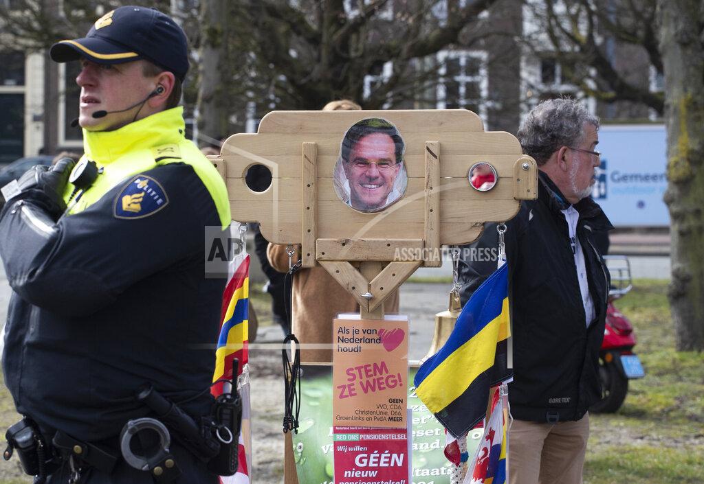 Peter Dejong A police man passes stocks with the head of caretaker Prime Minister Mark Rutte during a demonstration, ahead of three days of voting starting Monday in a general election, to protest government policies including the curfew, lockdown and coronavirus related restrictions in The Hague, Netherlands, Sunday, March 14, 2021. (AP Photo/Peter Dejong)