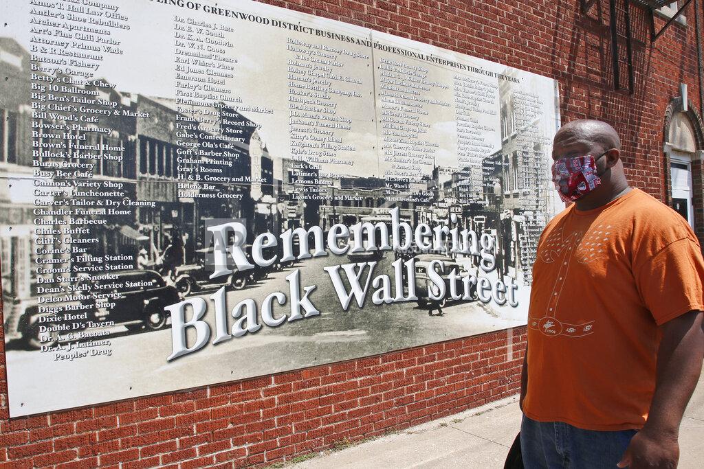 Sue Ogrocki Freeman Culver stands in front of a mural listing the names of businesses destroyed during the Tulsa race massacre in Tulsa, Okla., Monday, June 15, 2020, on the other side of what's historically the city's white-black dividing line from where President Donald Trump will rally Saturday. (AP Photo/Sue Ogrocki)