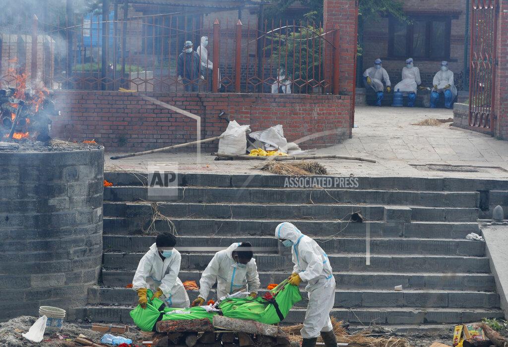 Niranjan Shrestha Nepalese workers wearing personal protective suits place the body of a COVID-19 victim on a funeral pyre for cremation on the banks of Bagmati river in Kathmandu, Nepal, Friday, May 7, 2021. Across the border from a devastating surge in India, doctors in Nepal warned Friday of a major crisis as daily coronavirus cases hit a record and hospitals were running out of beds and oxygen. (AP Photo/Niranjan Shrestha)