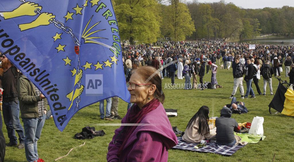 Olivier Matthys A woman stands next to a flag as people gather at the Bois de la Cambre park for a party called "La Boum 2" in Brussels, Saturday, May 1, 2021. Police put on extra patrols Saturday to monitor the gathering which is being held in defiance of Belgium's current COVID-19 regulations. (AP Photo/Olivier Matthys)
