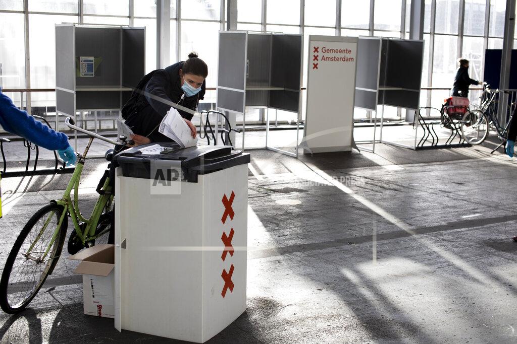 Peter Dejong A woman casts her ballot in ride through polling station for bicycles in Amsterdam, Netherlands, Monday, March 15, 2021. Polling stations opened across the Netherlands early Monday in a general election that has been spread over three days to allow people to vote safely during the coronavirus pandemic. (AP Photo/Peter Dejong)