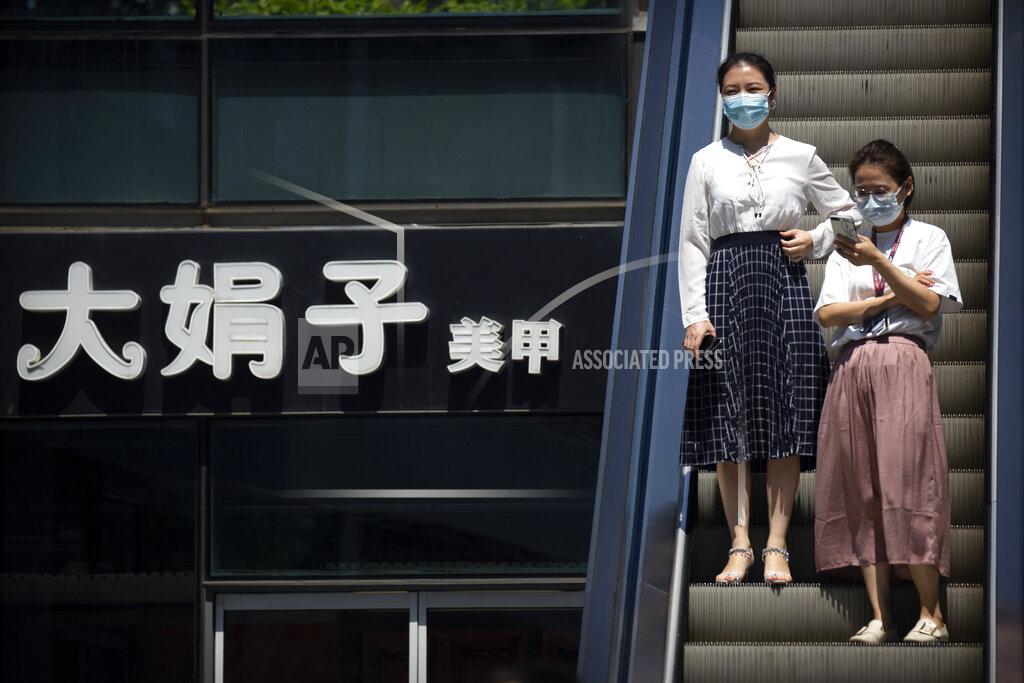 Mark Schiefelbein People wearing face masks to protect against the coronavirus ride an escalator past a sign of a nail salon at a shopping and office complex in Beijing, Tuesday, Aug. 11, 2020. Mainland China and semi-autonomous Hong Kong saw declines in their recent outbreaks Tuesday. (AP Photo/Mark Schiefelbein)