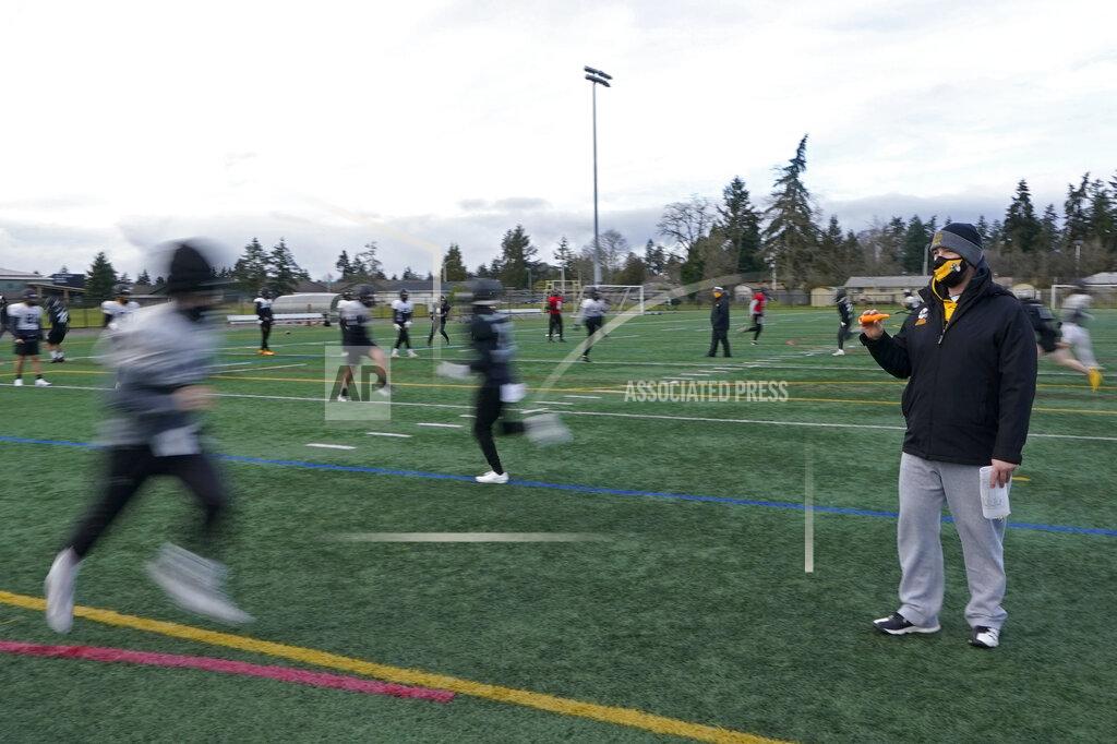 Ted S. Warren Brant McAdams, right, football coach at Pacific Lutheran, uses an electronic push-button whistle to guide players as they run socially distanced drills during practice Tuesday, Feb. 2, 2021, on campus in Tacoma, Wash. The whistle, which is more hygienic than traditional ones that are blown, is one of many measures taken by PLU and other schools to try and prevent the spread of COVID-19. For all the attention heaped on the FBS level of college football last fall as it tried to play, it will not be the only college football during the 2020-21 sports calendar as a handful of NCAA Division III and NAIA programs begin some form of a winter/spring season Saturday, Feb. 6. (AP Photo/Ted S. Warren)