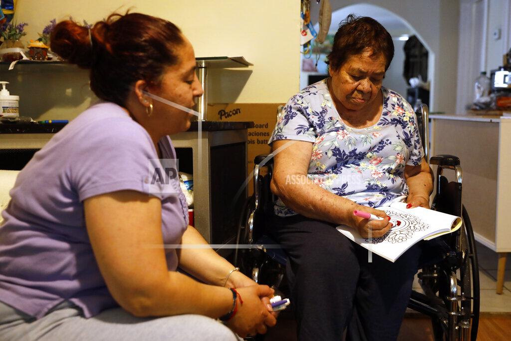 Shafkat Anowar Eugenia Rodriguez, left, looks toward her 84-year-old, non-citizen mother, Francisca Perez, who colors a book, a part of her regular exercise to recover rheumatoid arthritis, Wednesday, June 30, 2021, in their house in Chicago's Little Village neighborhood. Rodriguez hasn't been eligible for insurance coverage after overstaying a visitor visa from Mexico. She used to wake up every two or three hours at night to check on her mother. Since getting health insurance through the Illinois program, her mother has all the medications she needs. (AP Photo/Shafkat Anowar)