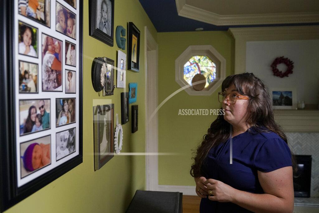 Steven Senne Allison Cullen, of Brockton, Mass., views a wall covered with family photo while speaking with reporters, Thursday, July, 22, 2021, at her home in Brockton. Cullen's husband Flavio Andrade Prado, a Brazilian national Prado is being held by Immigration and Customs Enforcement, or ICE, at the Plymouth County House of Corrections. Cullen, a mother of two, says she and her children haven't been able to visit her husband since before the pandemic. (AP Photo/Steven Senne)